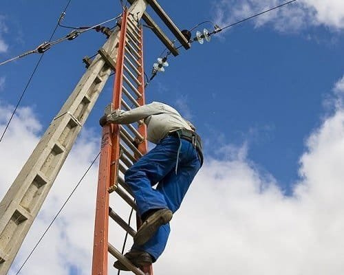 Electricista utilizando una escalera telescópica para revisar la instalación de un poste